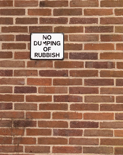 A rectangular sign with a wooden frame and a black background displays the message 'No Smoking In This Area' in large white letters, positioned on a sidewalk outside a commercial building. Behind the 
